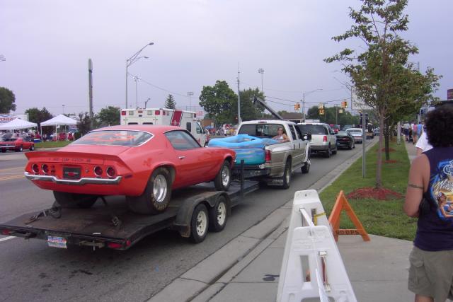 A girl, in a kiddie-pool, in the bed of a pickup that's towing a flatbed that's carrying a Camaro